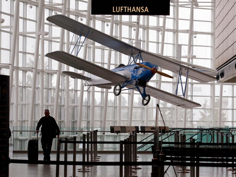 An airline traveler walks in view of a 1926 Alexander Eaglerock Combo-Wing airplane displayed at Seattle-Tacoma International Airport in SeaTac, Wash.