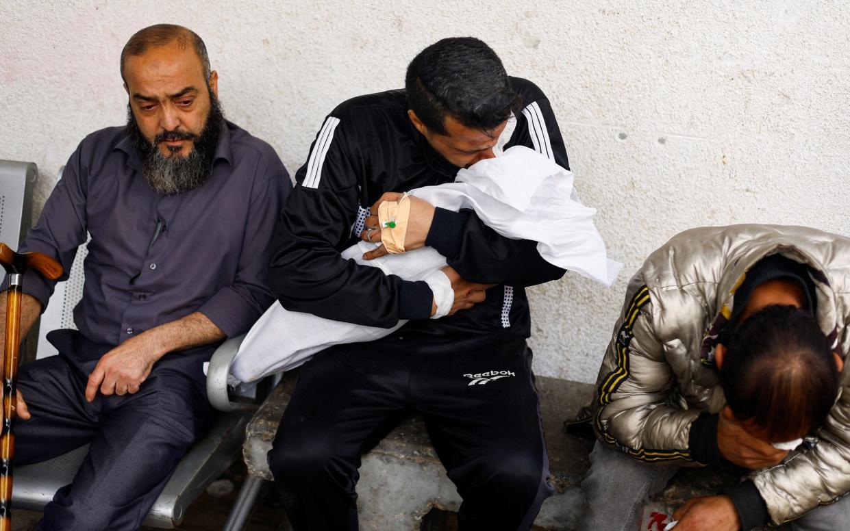 A Palestinian man from the Daraz family reacts while holding the body of his child who was killed in an Israeli strike