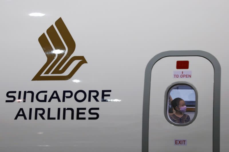 FILE PHOTO: A girl wearing a Singapore Airlines cabin crew uniform is pictured through a window of a replica aircraft during a guided tour at the Singapore Airlines Training Centre in Singapore