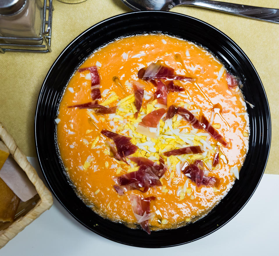 A bowl of soup garnished with cheese and ham pieces