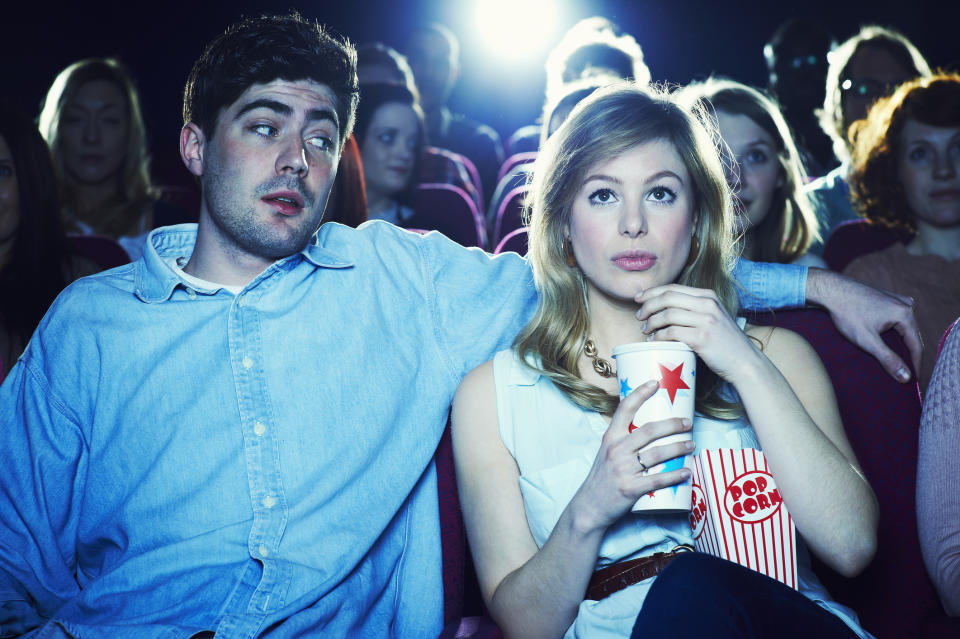 A man and woman sitting close in a movie theater, the man has an arm around the woman