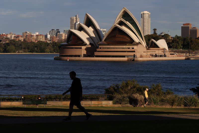 People stroll through a park in front of the Sydney Opera House in Sydney