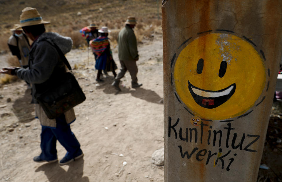 Residents walk past a cement post decorated with a smiley face and a message that reads in Uru; “I’m happy,” in the Urus del Lago Poopo indigenous community, in Punaca, Bolivia, Monday, May 24, 2021. None of the inhabitants speak Uru, the language of their ancestors. However, in the past few years they have decided to recover their native language. (AP Photo/Juan Karita)