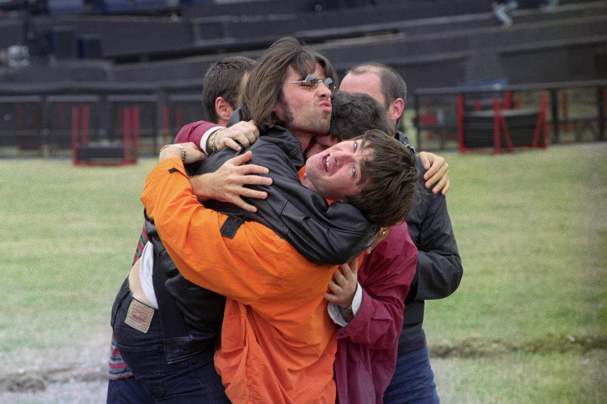 Liam, left, and Noel Gallagher, in orange, with other members of Oasis hug it out at Knebworth Park in 1996.