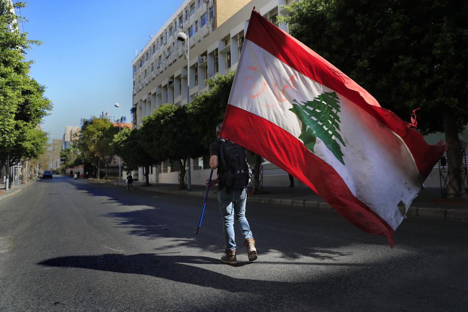 A protester holds a Lebanese flag, as he walks on a blocked main road that leads to the Central Bank during a protest against the increase in prices of consumer goods and the crash of the local currency, in Beirut, Lebanon, Tuesday, March 16, 2021. Scattered protests broke out on Tuesday in different parts of the country after the Lebanese pound hit a new record low against the dollar on the black market. (AP Photo/Hussein Malla)