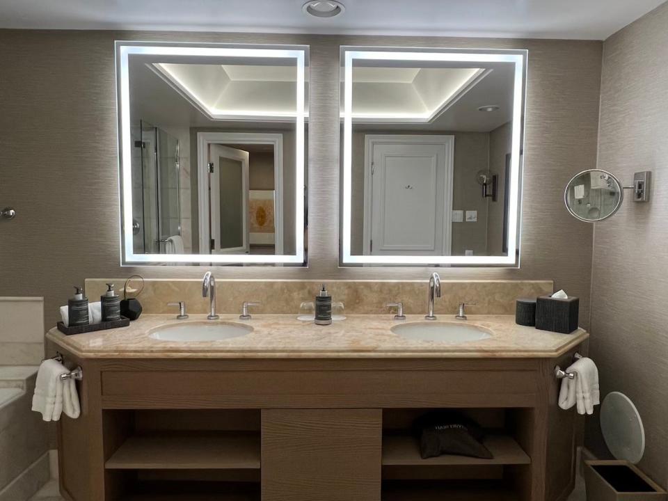 A bathroom vanity with double sinks and LED mirrors inside a guestroom at the Four Seasons Maui at Wailea.