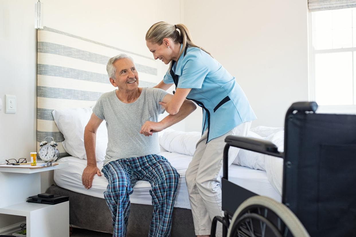 nurse helping old patient get up out of bed