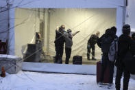 Royal Canadian Mounted Police, left, search migrants after their arrival at a reception center for irregular borders crossers, in Saint-Bernard-de-Lacolle, Quebec, in Canada, Wednesday Jan. 12, 2022, in a photo taken from Champlain, N.Y. The process was halted for most cases after the 2020 outbreak of COVID-19, but the Canadian government changed its policy in November, allowing the process to resume. (AP Photo/Wilson Ring)