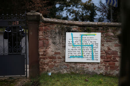 A French gendarme stands at a gate near a plaque desecrated with a swastika at the Jewish cemetery in Quatzenheim, near Strasbourg, France, February 19, 2019. REUTERS/Vincent Kessler