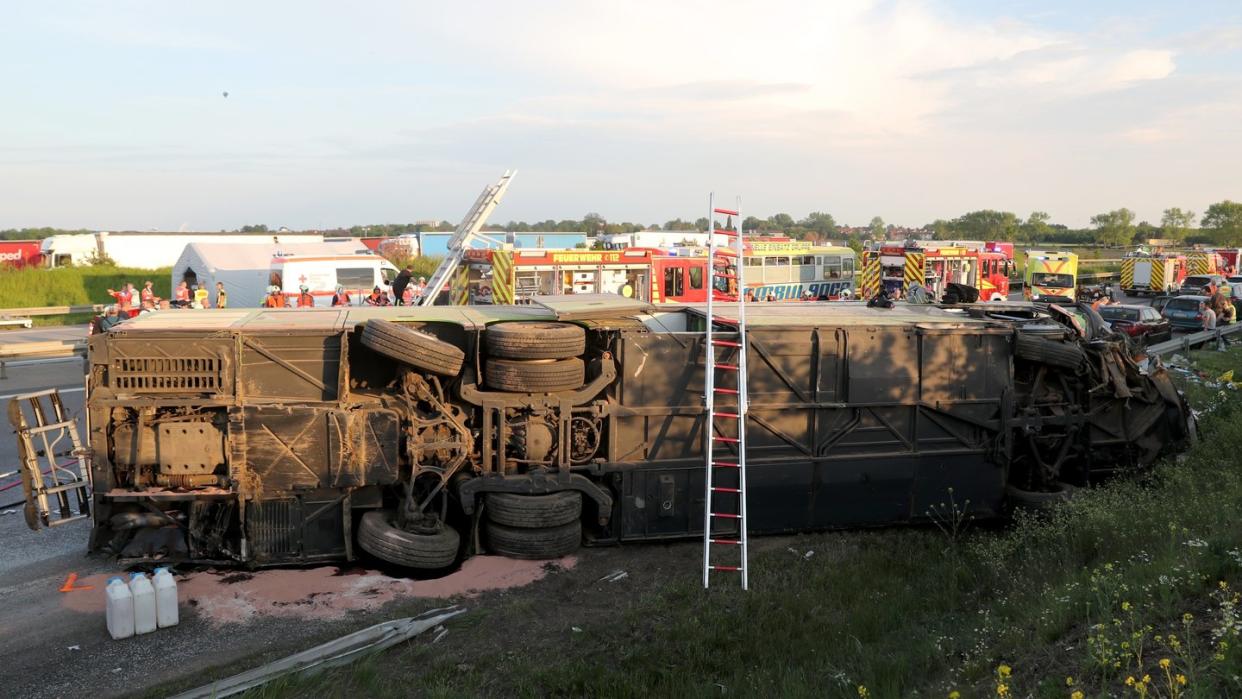 Einsatzkräfte der Feuerwehr stehen an der Unfallstelle neben dem verunglückten Bus. Der Bus überschlug sich zwischen den Anschlussstellen Leipzig-West und Bad Dürrenberg. Anschließend blieb das Fahrzeug auf der Seite liegen. Foto: Jan Woitas