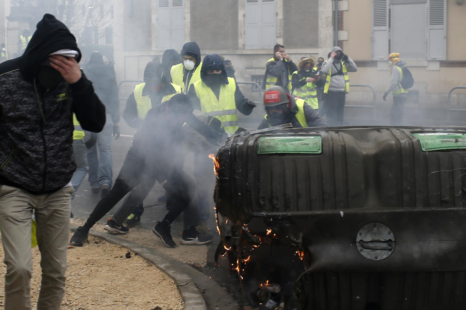 A man rubs his eyes as others set up barricades in a cloud of tear gas during demonstration in Bourges, central France, Saturday, Jan. 12, 2019. Paris brought in armored vehicles and the central French city of Bourges shuttered shops to brace for new yellow vest protests. The movement is seeking new arenas and new momentum for its weekly demonstrations. Authorities deployed 80,000 security forces nationwide for a ninth straight weekend of anti-government protests. (AP Photo/Rafael Yaghobzadeh)