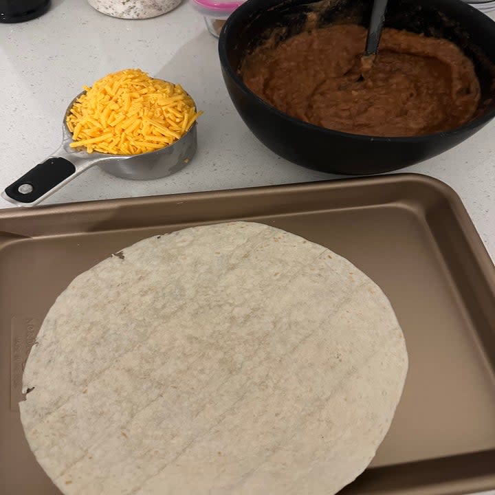 a cup of cheese, a tortilla, and beans/salsa mixture on the counter