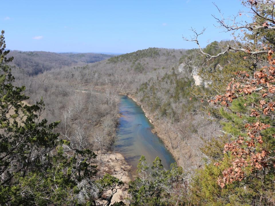 calm blue and brown river cuts through hills of bare trees