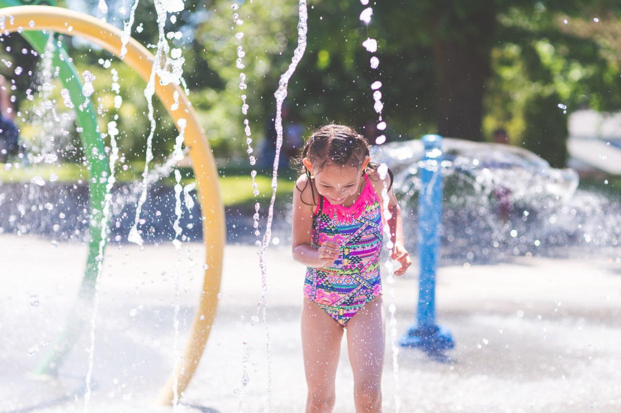 A young girl in a swimsuit ducks and runs through the neighborhood splash pad on a hot summer day.