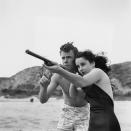 <p>Elizabeth gets a lesson from fellow actor Marshall Thompson on how to use a shot gun during a day at the beach. </p>