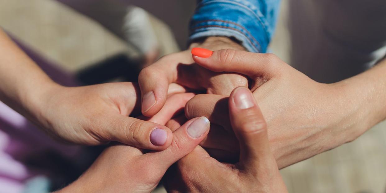 two man and three women holding hands on a table implying a polyamory relationship or love triangle