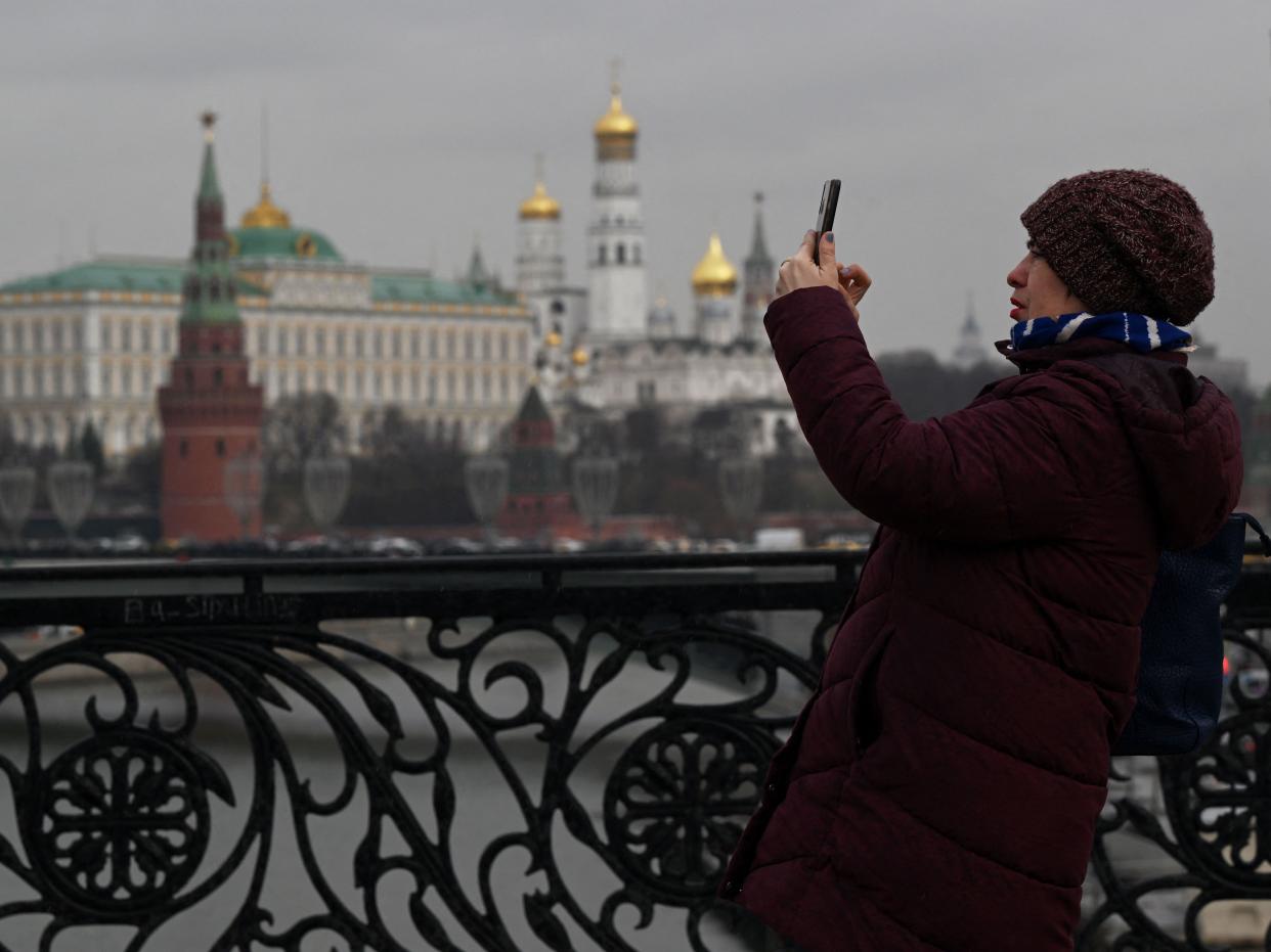 A woman takes pictures with a smartphone standing on the pedestrian Patriarchal Bridge over the Moskva river, with the Kremlin seen in the background, in central Moscow on March 21, 2023, ahead of a meeting of Russian President and his Chinese counterpart.
