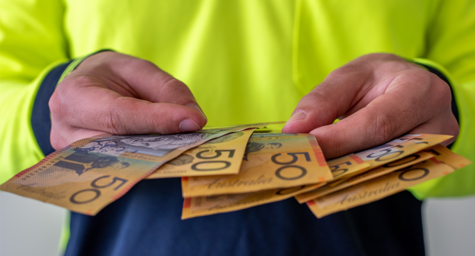 An Australian tradesman holds cash in his hands.