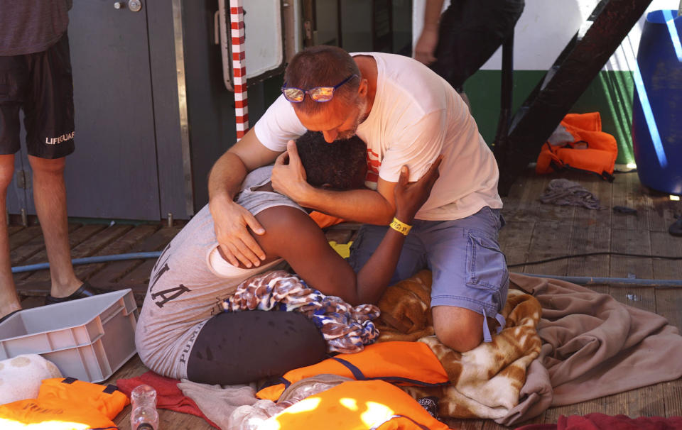 A migrant is comforted by a crew member of the Open Arms Spanish humanitarian boat off the coast of the Sicilian island of Lampedusa, southern Italy, Sunday, Aug.18, 2019. An Open Arms spokeswoman tells The Associated Press that the humanitarian group is not willing to sail to Spain's southernmost Algeciras port given the emergency situation that they are experiencing inside the boat. (AP Photo/Francisco Gentico)