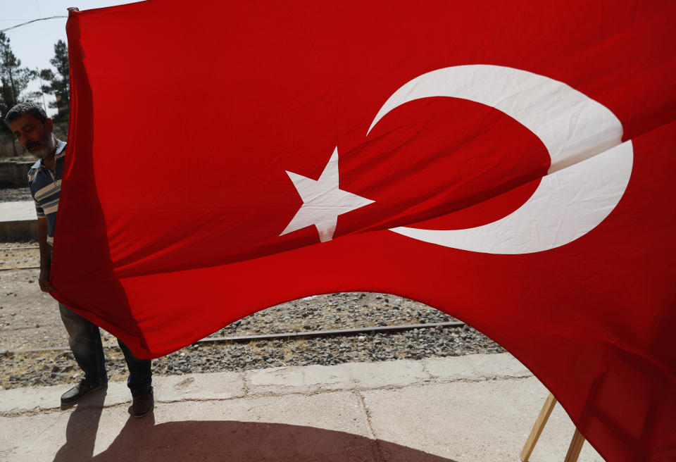 A man holds a Turkish flag at the border between Turkey and Syria, in Akcakale, Sanliurfa province, southeastern Turkey, Tuesday, Oct. 8, 2019. The Turkey - Syria border has became a hot spot as Turkish Vice President Fuat Oktay said Turkey was intent on combatting the threat of Syrian Kurdish fighters across its border in Syria.(AP Photo/Lefteris Pitarakis)