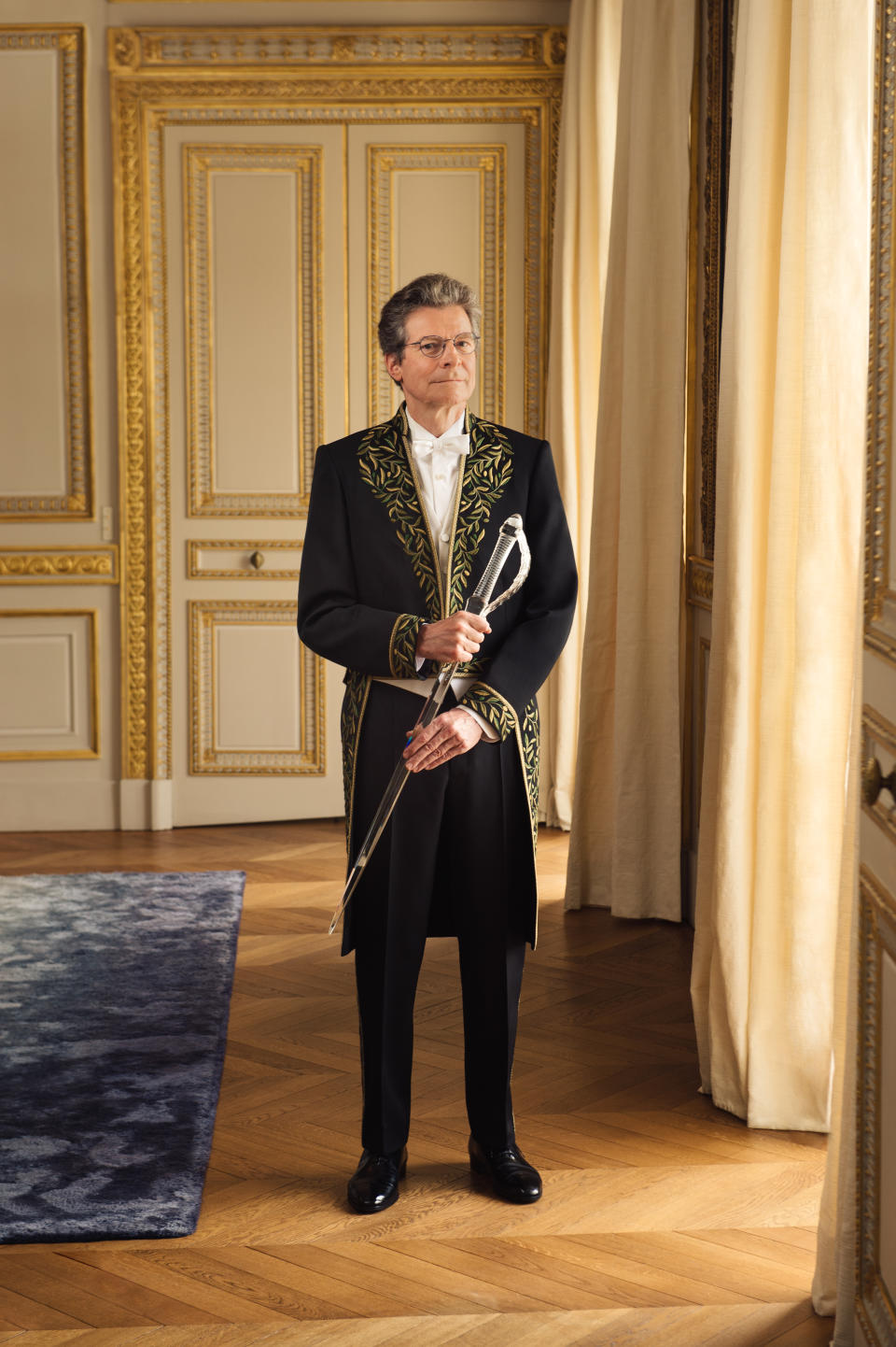 Antoine Compagnon stands in an opulent room with gold molding wearing ceremonial garb by Balenciaga.