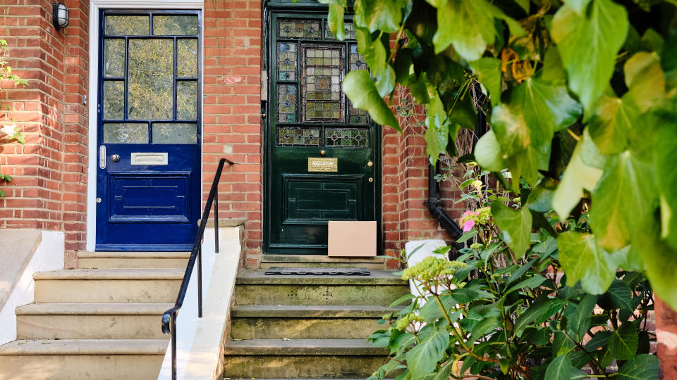 A delivery box sits on the stairs of a front door of a picturesque vintage house, in a luxurious London neighborhood, presenting a modern convenience within a traditional setting.