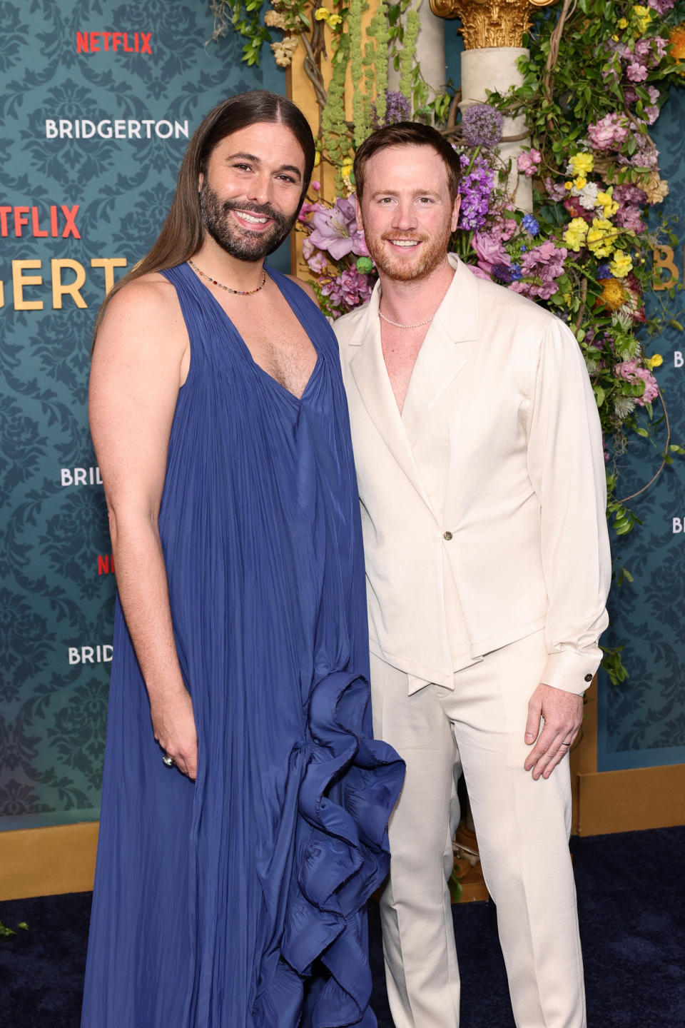 Jonathan Van Ness in a flowing dress and Mark Peacock in a suit at a Netflix Bridgerton event