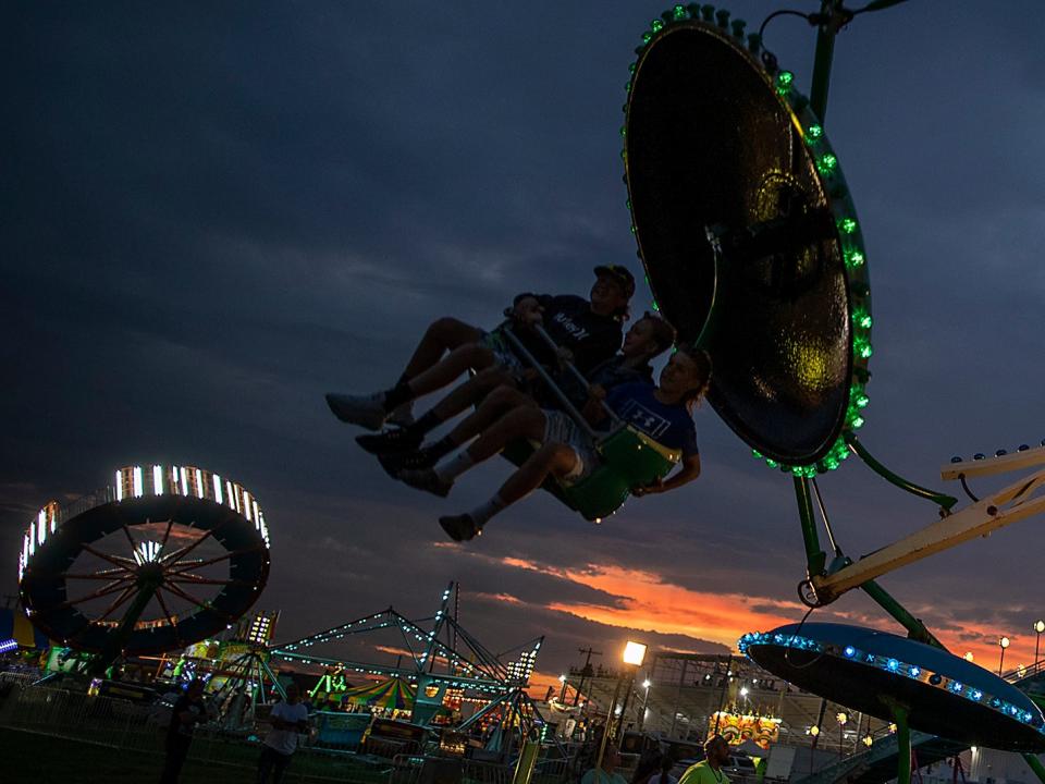 A trio of riders on the paratrooper ride are silhouetted against the sky on the midway of the Knox County Fair on Wednesday, July 7, 2021.