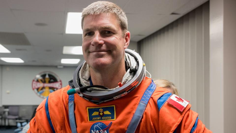 smiling Jeremy Hansen in an orange spacesuit at a NASA facility