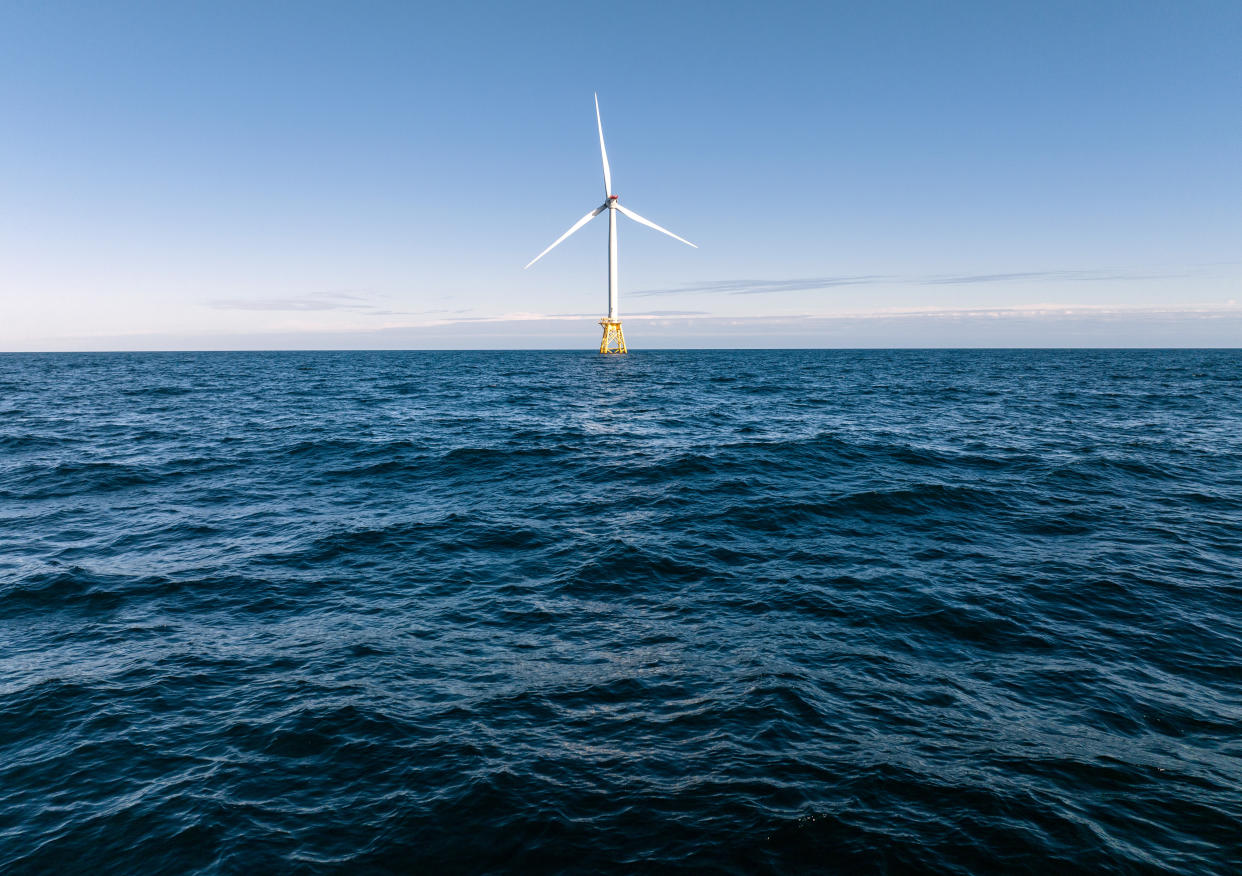 Large three-blade wind turbine resting on a yellow platform on the ocean.