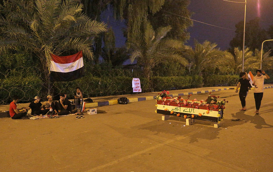 Anti-government protesters rest near a symbolic coffin bearing the colors of the national flag during a sit-in near the closed Najaf provincial council, in Najaf, Iraq, early Monday, Oct. 28, 2019. Protests have resumed in Iraq after a wave of anti-government protests earlier this month were violently put down. (AP Photo/Anmar Khalil)