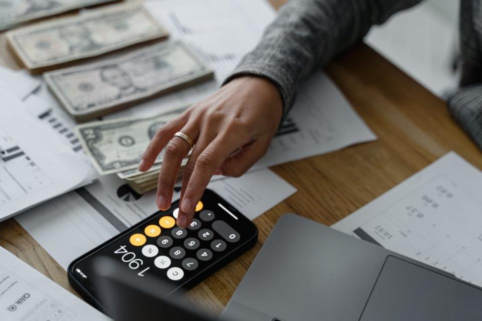 Hand of a person typing into a calculator near cash money on a table