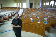 The Rev. Sean Horrigan, parish priest, stands in the sanctuary at Christ the Redeemer Catholic Church in front of photos of parishioners that are taped to the pews, which are part of virtual masses at the church, on Friday, April 10, 2020, in Houston. The coronavirus pandemic has shut down most religious services throughout the country and many churches are offering services through social media and video conferencing. (Brett Coomer/Houston Chronicle via AP)