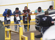 FILE - In this this Aug. 7, 2019, file photo, handcuffed workers await transportation to a processing center following a raid by U.S. immigration officials at Koch Foods Inc., plant in Morton, Miss. Federal officials announced Thursday, Aug. 6, 2020, the indictments of four executives from two Mississippi poultry processing plants on federal charges tied to one of the largest workplace immigration raids in the U.S. in the past decade. (AP Photo/Rogelio V. Solis, File)