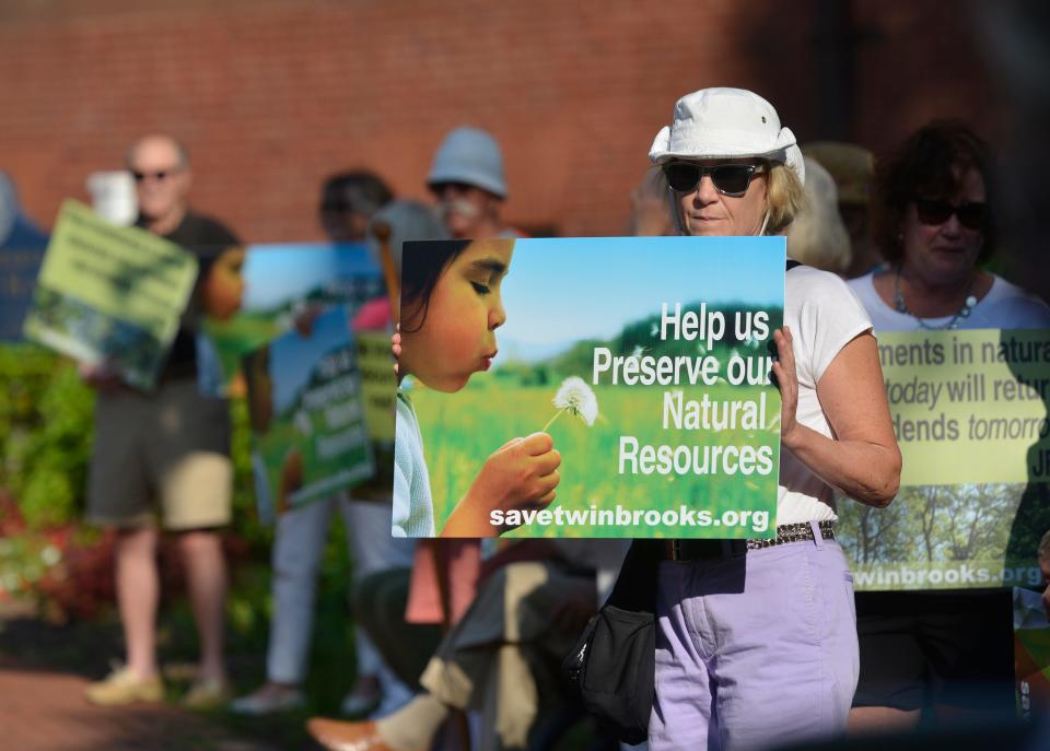 Jane Carlson, of Centerville and West Hyannisport, holds a sign outside Barnstable Town Hall on July 20, 2023, protesting plans to build a 312-unit housing project on 40 acres at Twin Brooks Golf Course. Faced with steady opposition from neighbors, the developer has dropped their plans.