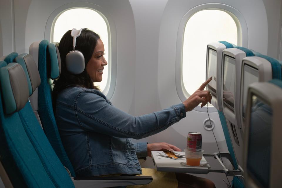 A woman with headphones touches a screen while seated in a main cabin seat in Hawaiian Airlines' new Boeing 787-9 Dreamliner.