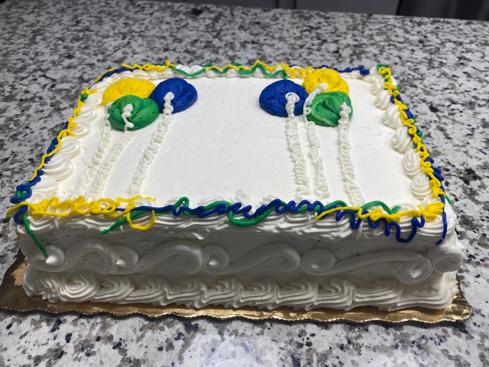 White sheet cake with blue, green, and yellow balloons piped on top  with white swirls on side