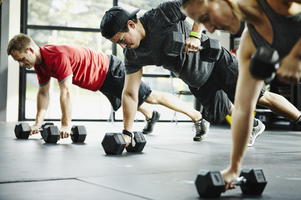 Group of friends doing pushups with dumbbells in gym gym