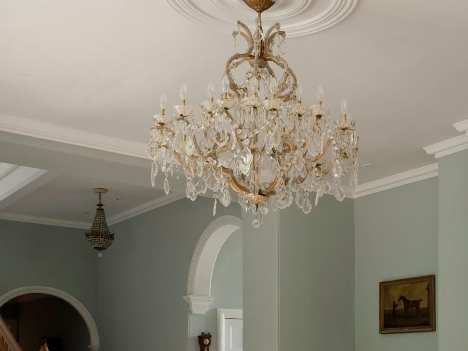 Room with green walls, fireplace, and dining table and chairs with crystal chandelier hanging from ceiling