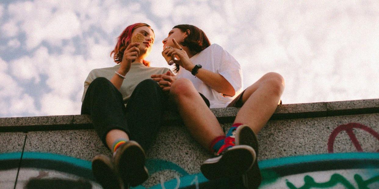 girlfriends eating ice cream while sitting in city during summer