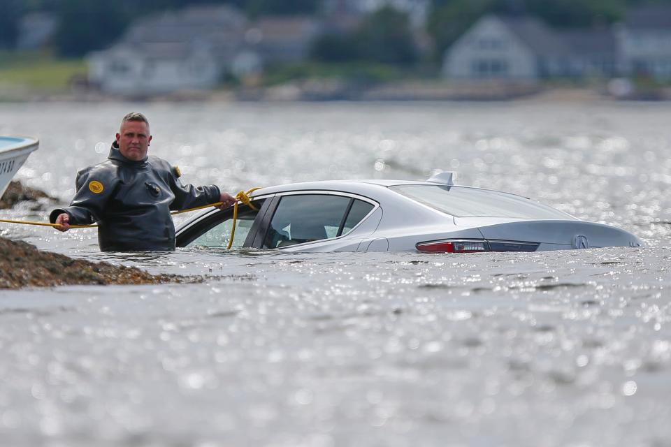 New Bedford Police officer Paul Fonseca helps to tie a rope to a car that ended up in the water off of West Beach in New Bedford after the motorist became distracted by a bee.