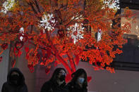 Residents wearing masks to protect from the coronavirus walks near decorative lights on a tree in Beijing, China, Thursday, Jan. 20, 2022. The sweeping "zero-tolerance" policies that China has employed to protect its people and economy from COVID-19 may, paradoxically, make it harder for the country to exit the pandemic. (AP Photo/Ng Han Guan)