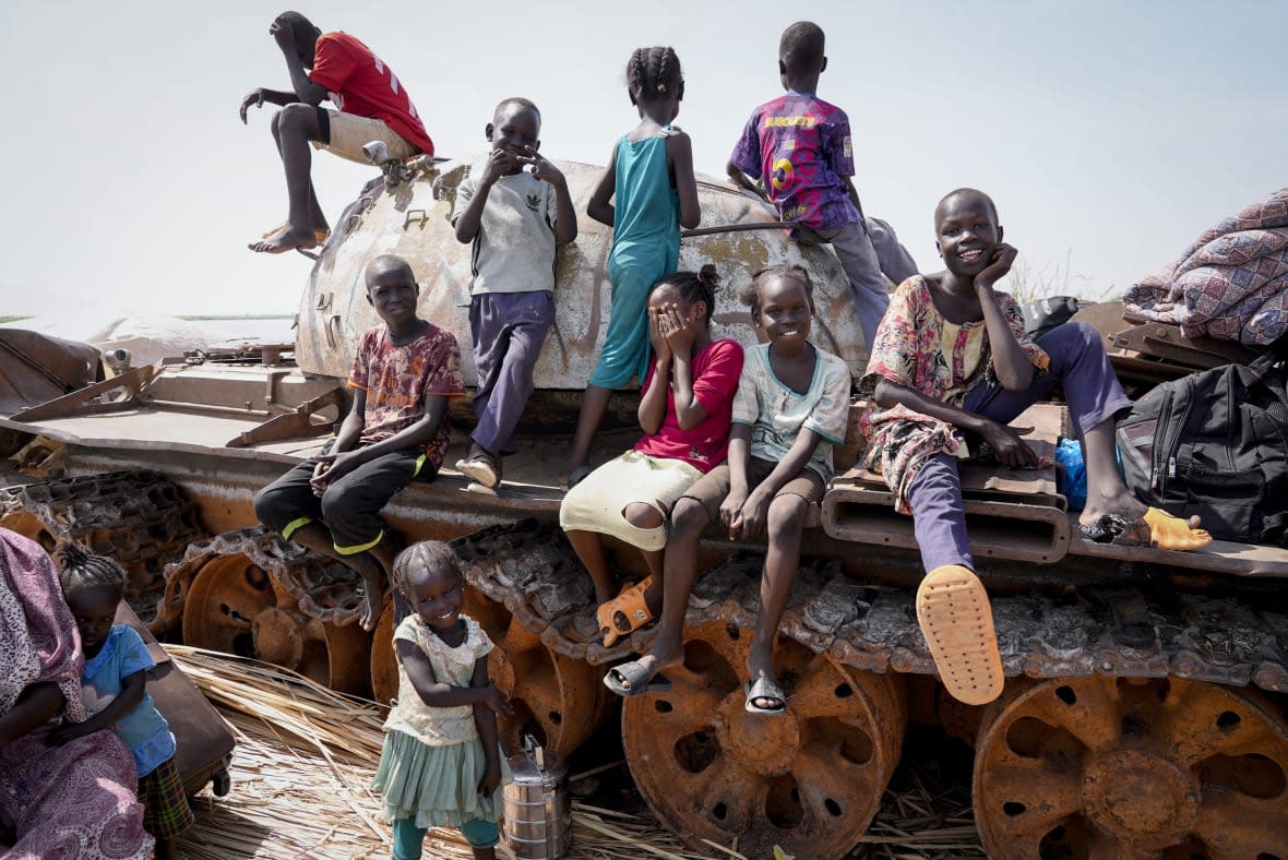 Children sit and play on the remains of a tank, at the river port in Renk, South Sudan Wednesday, May 17, 2023. Tens of thousands of South Sudanese are flocking home from neighboring Sudan, which erupted in violence last month. (AP Photo/Sam Mednick)