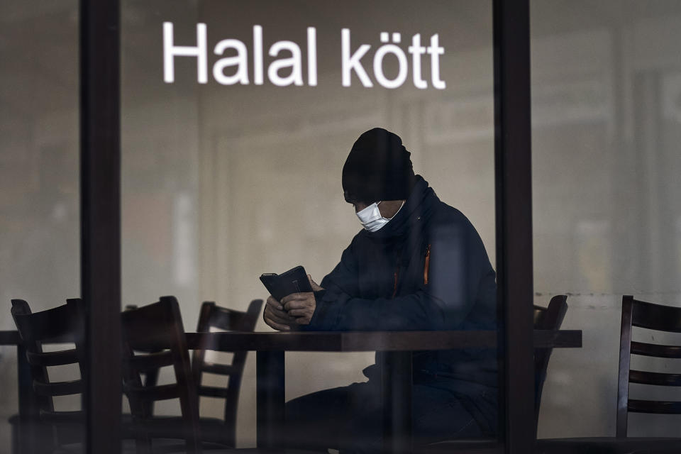 A man sits at a restaurant in Rinkeby district, Rinkeby-Kista borough in Stockholm, Sweden, Tuesday, April 28, 2020. The coronavirus has taken a disproportionate toll among Sweden's immigrants. Many in these communities are more likely to live in crowded households and are unable to work remotely. There also are concerns the message has not reached everyone in immigrant neighborhoods. (AP Photo/Andres Kudacki)