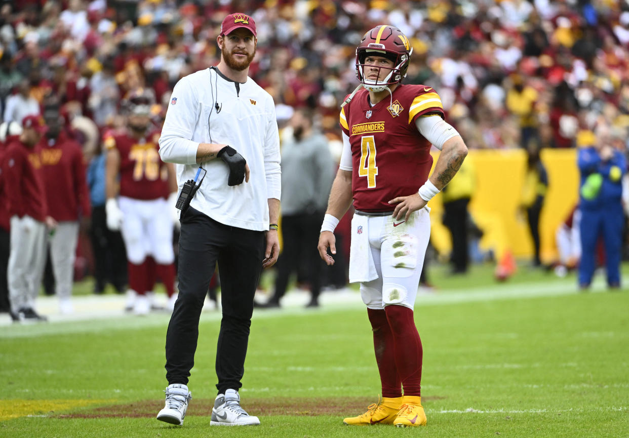 Oct 23, 2022; Landover, Maryland, USA; Washington Commanders quarterback Taylor Heinicke (4) talks with quarterback Carson Wentz against the Green Bay Packers during the first half at FedExField. Mandatory Credit: Brad Mills-USA TODAY Sports