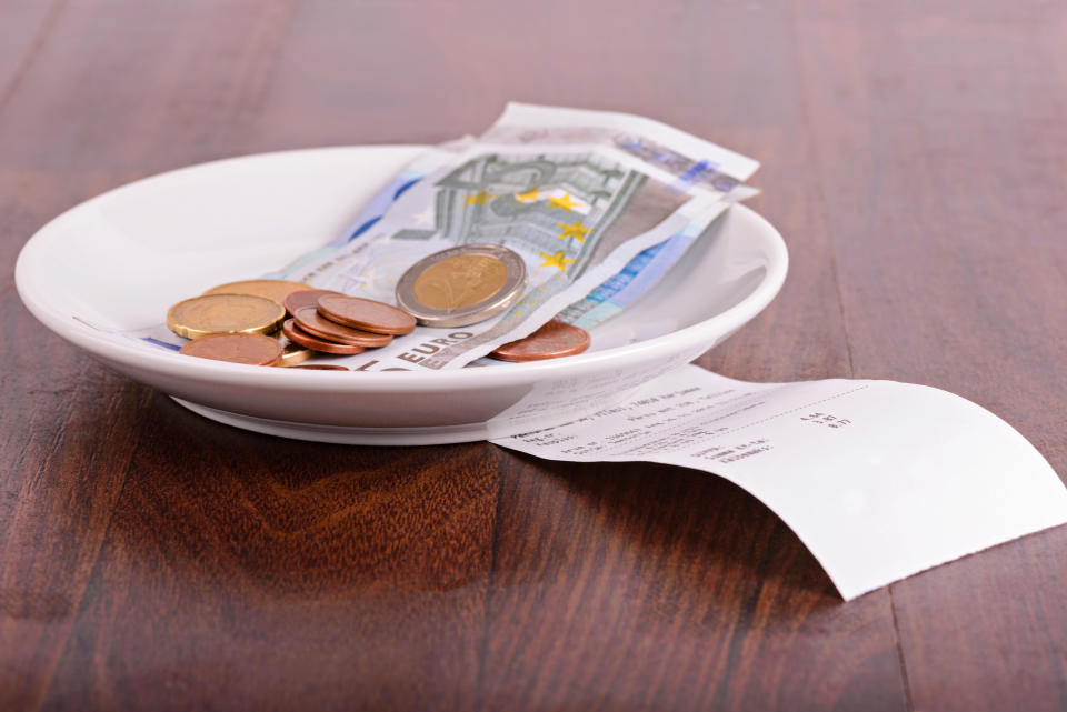 A white plate with several euro bills and coins on a wooden table next to a receipt