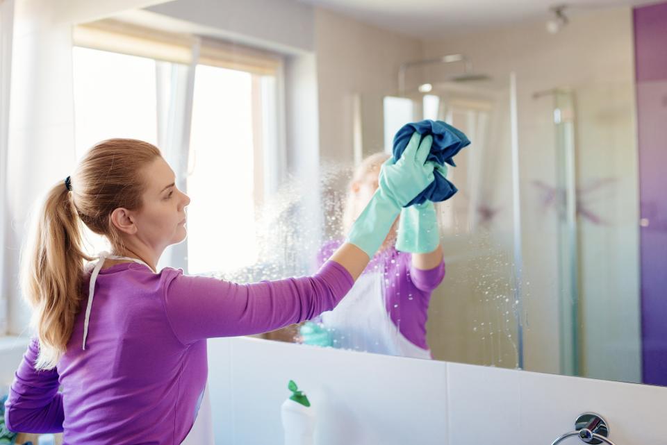 Young beautiful woman cleaning mirror in bathroom. Cleaning service. Maid cleaning at home