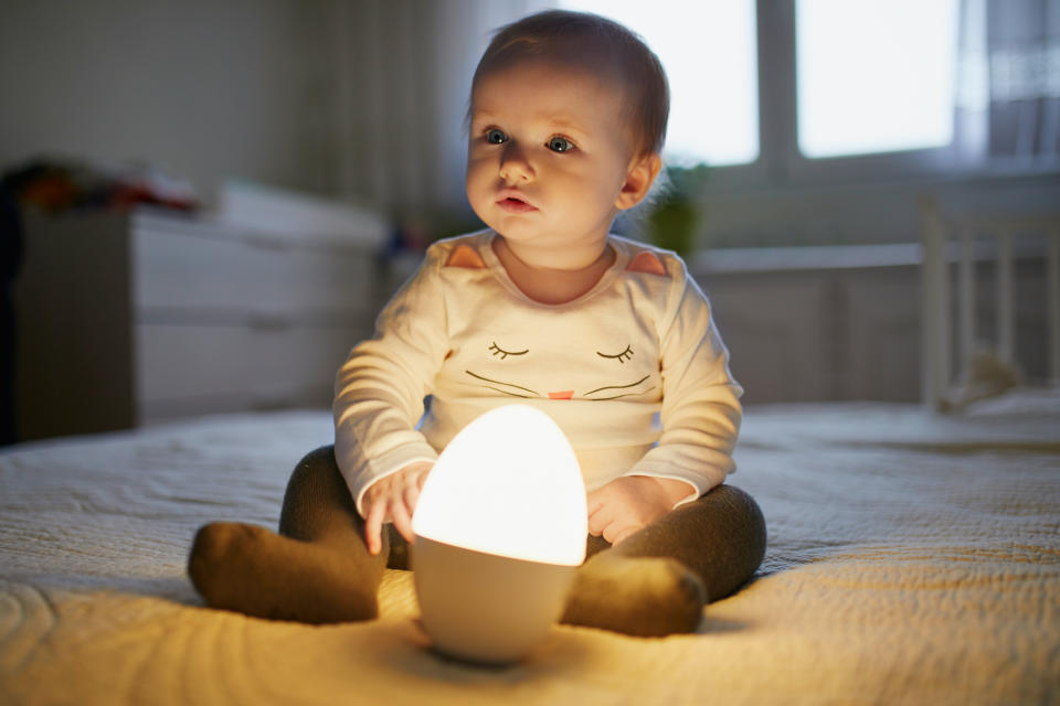 Adorable baby girl playing with bedside lamp in nursery