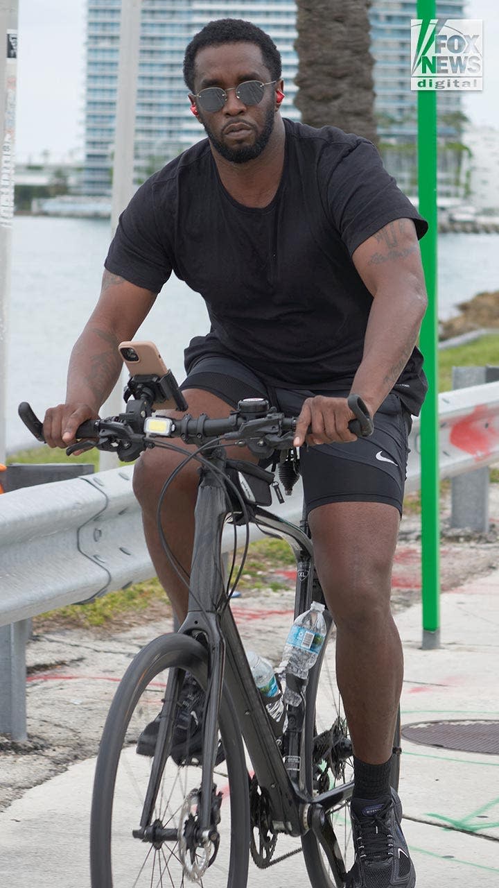 P Diddy looks at the camera wearing sunglasses as he rides his bicycle.