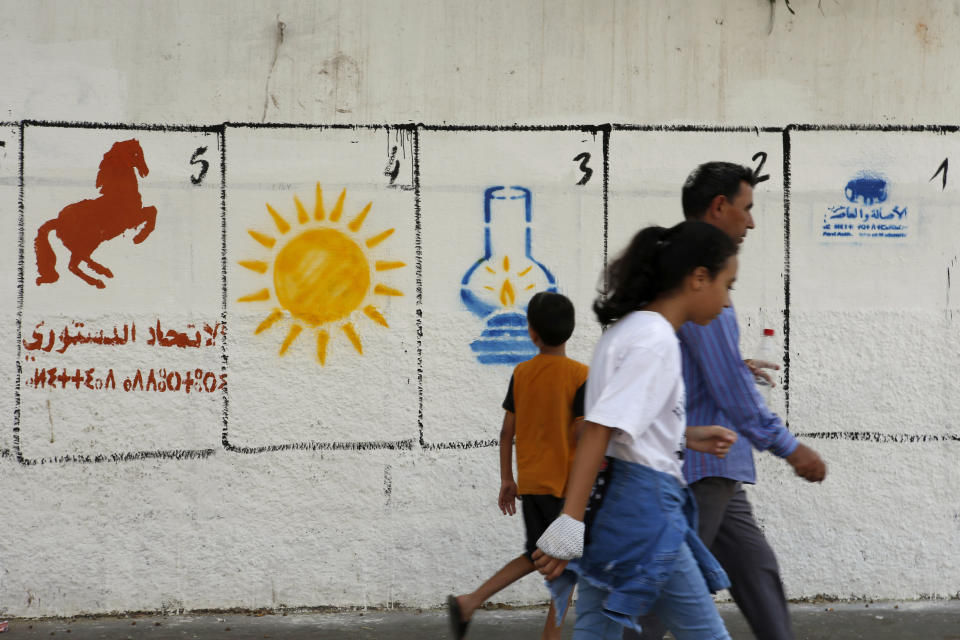 A Moroccan family walk past electoral paintings representing a political party logos for the upcoming municipal elections in Casablanca, Morocco, Tuesday, Sept. 7, 2021. Party logos are, from left, Constitutional Union (horse), "Renaissance and Virtue Party" (Sun), " Justice and Development Party" (Lamp), and at right "Authenticity and Modernity Party" (Tractor), at the El Fida district of Casablanca. To help illiterate people vote, only party logos will appear on ballot papers, and the numbers seen in the image are allocated to each party for displaying purposes only during the campaign. Elections are scheduled Wednesday 8. (AP Photo/Abdeljalil Bounhar)